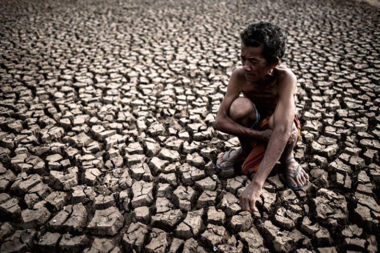 elderly-man-sitting-hugging-his-knees-bent-barren-ground-global-warming