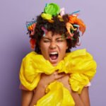 Headshot of irritated bothered young female wrapped in polythene sheeting, screams loudly, smirks face, keeps mouth widely, isolated on purple background. Stop using plastic. Recycling concept