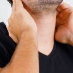 Young man suffering from neck pain in black t-shirt, cap , front view.