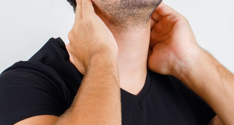 Young man suffering from neck pain in black t-shirt, cap , front view.