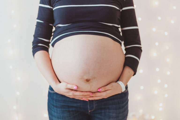 Close-up of pregnant woman's big hairy belly on bright bokeh lights background