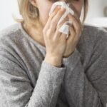 Sick woman sitting in bed, blowing nose with napkin