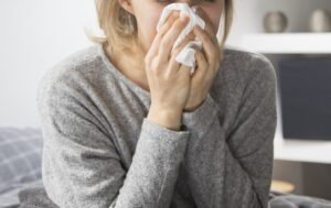 Sick woman sitting in bed, blowing nose with napkin